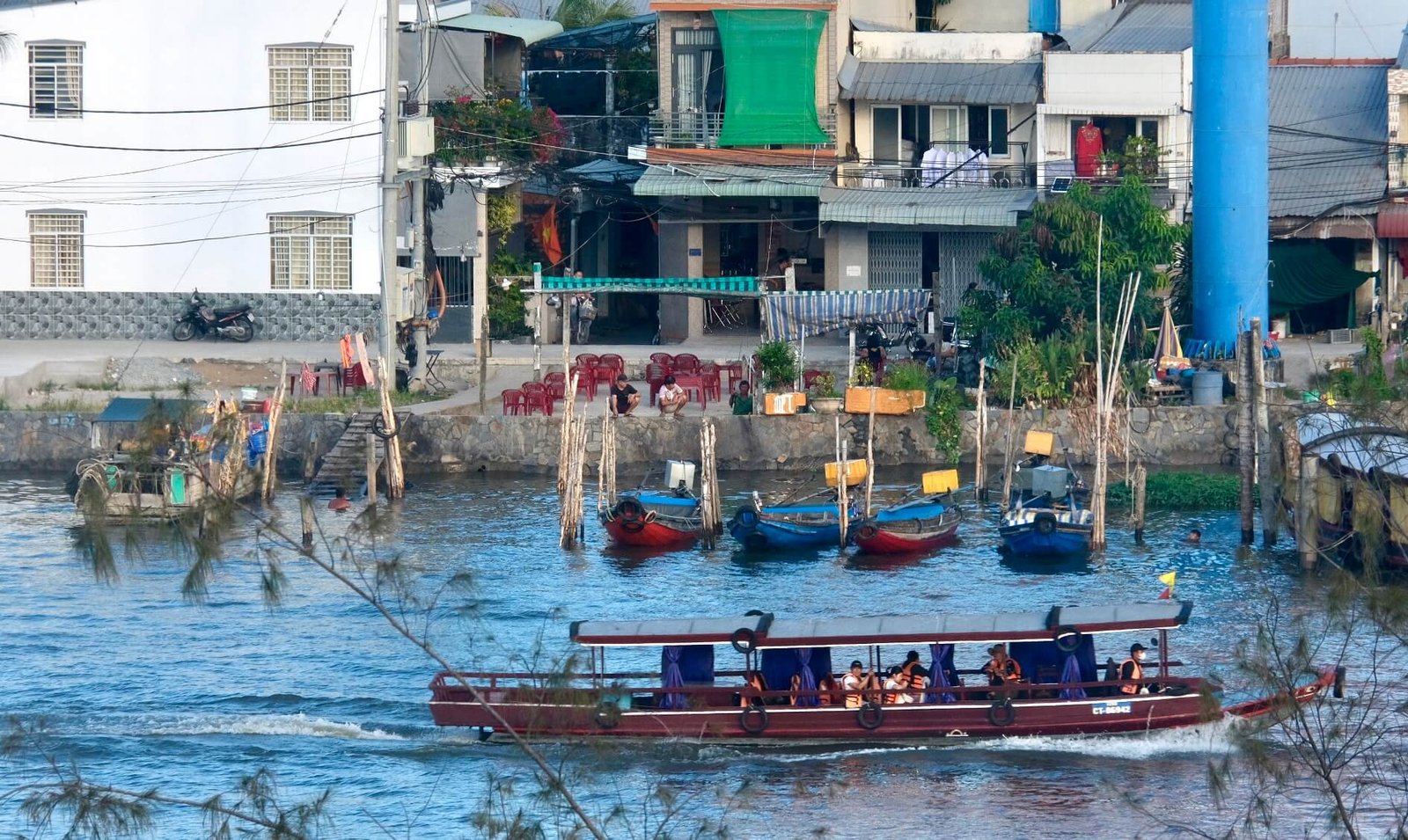 A tour boat carries passengers past a Mekong Delta riverside town near Can Tho, with fishing boats m
