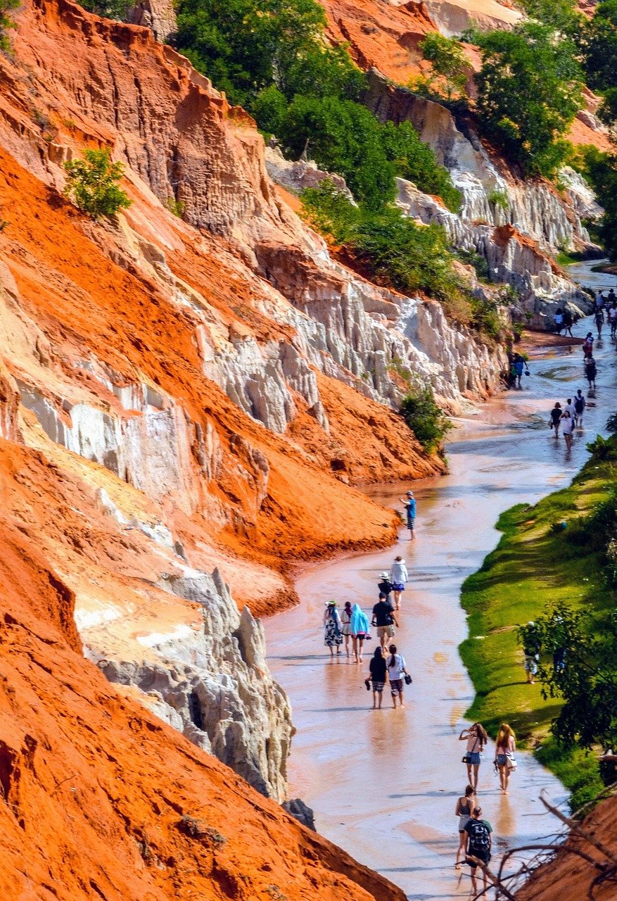 Tourists walking through the Fairy Stream (Suoi Tien) in Mui Ne with red sand cliffs on the left and