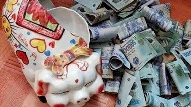 A broken ceramic piggy bank tipped on its side with Vietnamese dong banknotes spilling out across a 