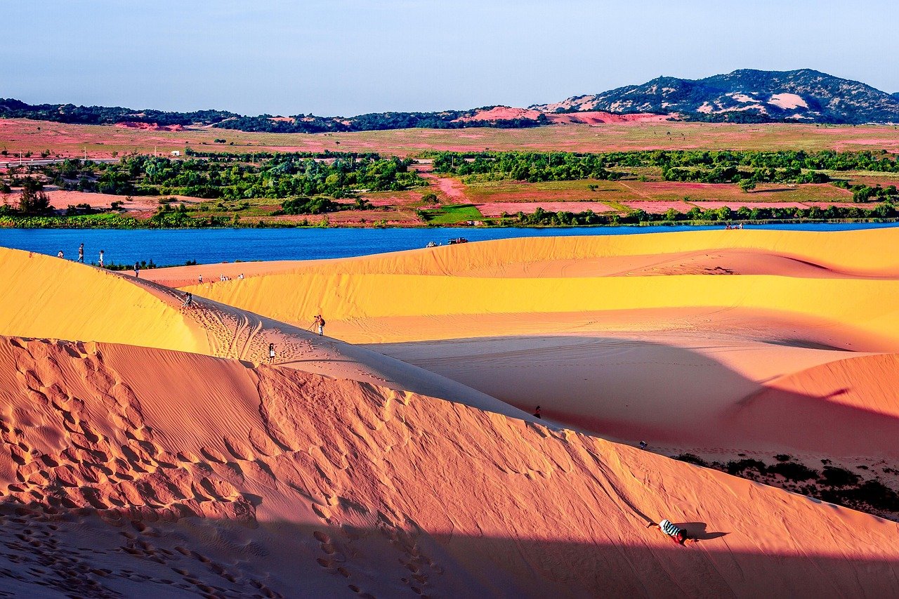 Wide landscape shot of Sand Dunes in Mui Ne Vietnam at sunrise with tiny tourists walking on t